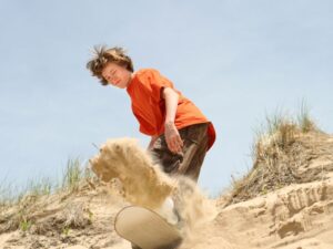 A person sandboarding down a steep, red sand dune under clear blue skies.